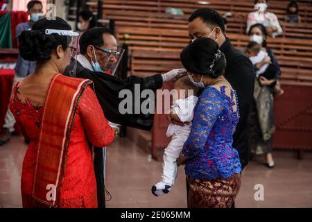 A priest wearing a face shield as a measure against the spread of Covid19  is seen laying his  hand on a toddler during the baptism ceremony of Christian congregation children at the Batak Karo Protestant Church in Medan. Stock Photo