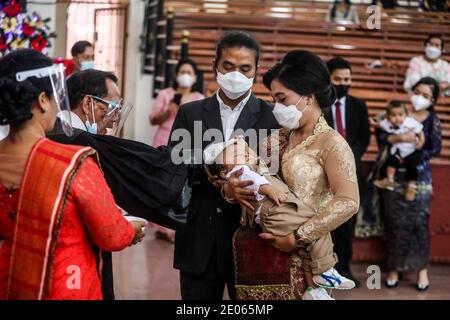 A priest wearing a face shield as a measure against the spread of Covid19  is seen laying his  hand on a toddler during the baptism ceremony of Christian congregation children at the Batak Karo Protestant Church in Medan. Stock Photo