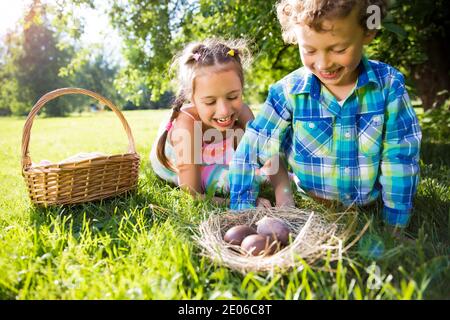 Cute boy and girl celebrating Easter, searching and eating chocolate eggs. Happy family holiday. Happy kids laughing, smiling and having fun. Stock Photo