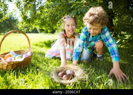 Cute boy and girl celebrating Easter, searching and eating chocolate eggs. Happy family holiday. Happy kids laughing, smiling and having fun. Stock Photo