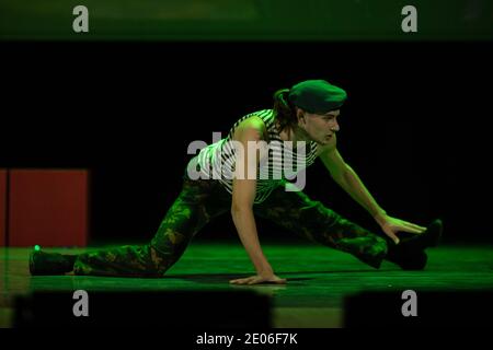 A young guy in military uniform is dancing on stage in a stage light. Stock Photo