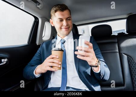 Smiling businessman using smartphone and holding disposable cup in car Stock Photo