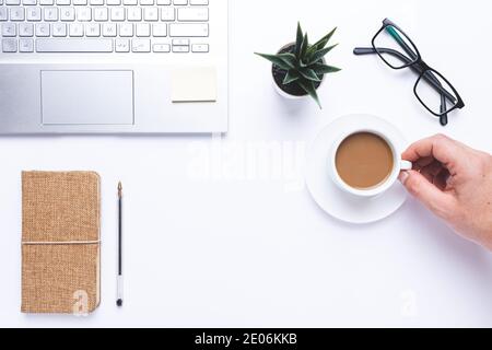 Flat lay, Workplace with laptop, hand taking coffe and notebook and pen on withe desk. Stock Photo