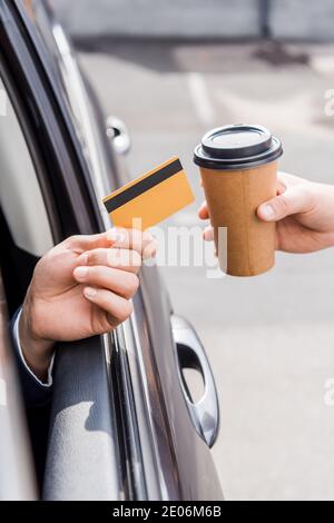 Cropped view of man holding credit card in auto near seller with takeaway coffee Stock Photo