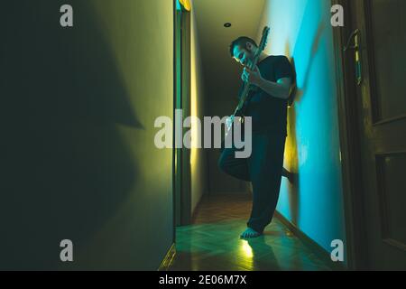 Caucasian man playing electric guitar at home. Colorful lighting. Stock Photo