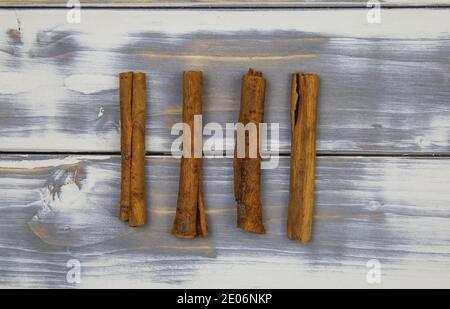 Top down view on four isolated cinnamon sticks on white natural wood table (focus on sticks) Stock Photo