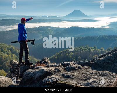 Photographer in silhouette carrying camera  on tripod. Natural photographer hold camera with tripod and watch to the misty mountain  valley Stock Photo