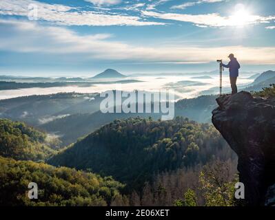 Photographer in silhouette carrying tripod with big camera. Natural photographer hold camera with tripod and watch to the misty mountain  valley Stock Photo