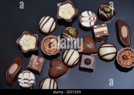 Close up of a selection of luxury chocolates, with a variety of shapes including a heart, florentines, and pistachios. They are in white, milk and dar Stock Photo