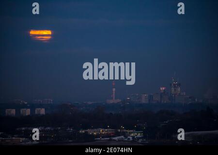 Birmingham, UK. 30th December, 2020. Early evening full moon breaking through the clouds as it begins its appearance rising over a snow-covered Birmingham city centre destined for its new Tier 4 restriction tomorrow. Credit: Lee Hudson/Alamy Live News