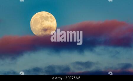 Full moon rising over pink clouds in blue sky Stock Photo