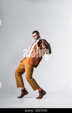 Man in terracotta jacket and brown pants holding bag on grey background Stock Photo