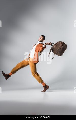 Fashionable man in terracotta jacket holding brown bag while walking on grey background Stock Photo