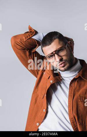 Bearded man in eyeglasses and terracotta jacket posing at camera isolated on grey Stock Photo