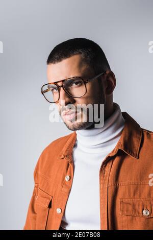 Trendy man in eyeglasses and terracotta jacket looking at camera isolated on grey Stock Photo