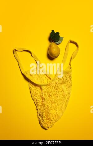 Quince apple fruit and yellow mesh bag on yellow background. Directly above view. Fruit and leaves have natural imperfections, spots and scratches. Ec Stock Photo