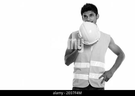 Young handsome Indian man construction worker covering face with safety helmet while thinking Stock Photo