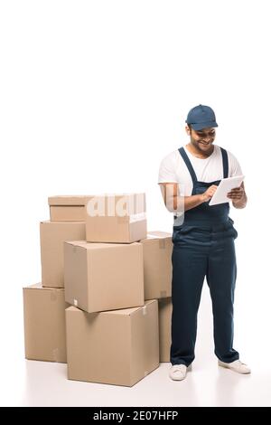 happy indian mover in overalls using digital tablet near carton boxes on white Stock Photo