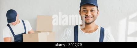 cheerful indian worker looking at camera near coworker on blurred background, banner Stock Photo