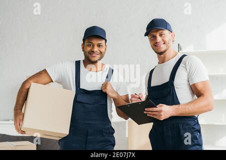 cheerful multicultural movers smiling while looking at camera in apartment Stock Photo