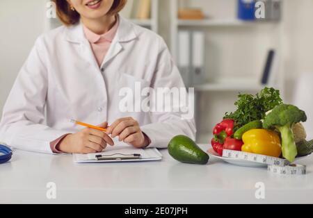 Dietitian sitting at table with fresh fruit, vegetables and individual diet plan Stock Photo