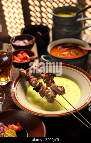 Sate Klatak, the Javanese Lamb Satay on Bicycle Spoke Skewer, Served with Yellow Curry Soup and Condiment of Shallot, Tomato, Chili Sauce, Soy Sauce Stock Photo