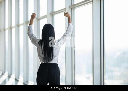 Confident businesswoman spreading hands standing at office window, enjoying big city, successful entrepreneur celebrating business success with arms o Stock Photo