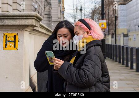 London, UK. 30th Dec, 2020. Women use a smartphone of the street.As daily Covid19 infection rate hits record high in London, the government is pinning its hopes on the Oxford/AstraZeneca jab. Credit: SOPA Images Limited/Alamy Live News Stock Photo