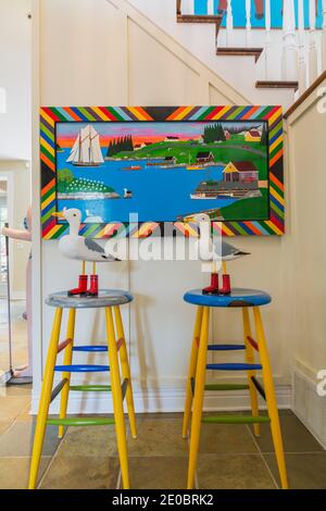 Yellow, blue and green folk art bar stools and seagulls with red boots next to oak wood staircase with white painted balustrades leading to upstairs Stock Photo