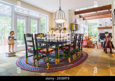 Colourful acrylic painted pine wood dining table with high back chairs on weaved checkered oval rug in dining room with earth-toned ceramic tiles Stock Photo