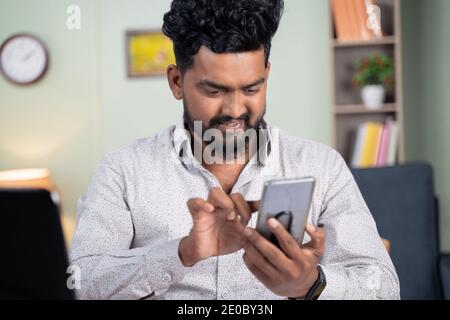 young man smiling by reading funny message or sms on mobile phone at office - Concept of using social media, Internet and entertainment lifestyle. Stock Photo