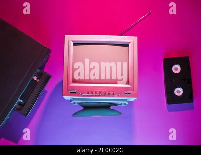 Retro wave, 80s concept. Video player with vhs cassette, old tv, neon light. Top view, flat lay Stock Photo
