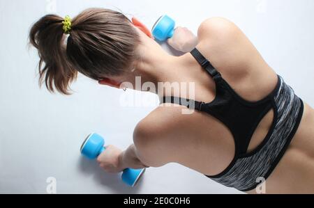 Young fit woman in sportswear getting ready to do pushups with dumbbells on white background. Top view Stock Photo