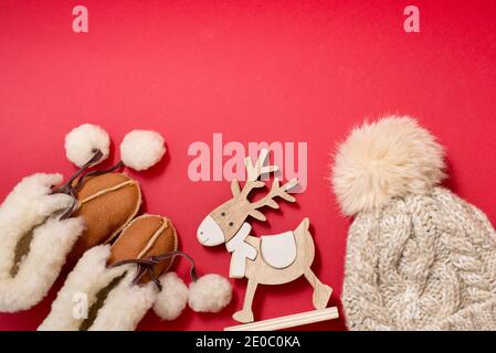 Baby winter clothes booties and hat on red background with wood toy deer, copy space Stock Photo