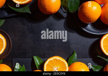Backgroung with Oranges, orange slices and orange leaves on black textured background Stock Photo
