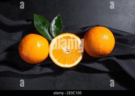 Oranges, orange slice and orange leaves on black textured background Stock Photo