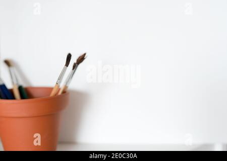 A pot of artists paint brushes in a browm pot on a white background. Copy space available. Stock Photo
