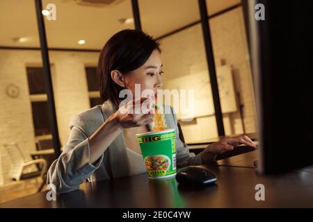 Young woman in the office to work overtime to eat instant noodles Stock Photo