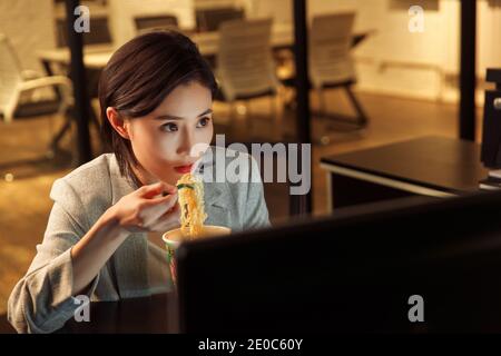 Young woman in the office to work overtime to eat instant noodles Stock Photo