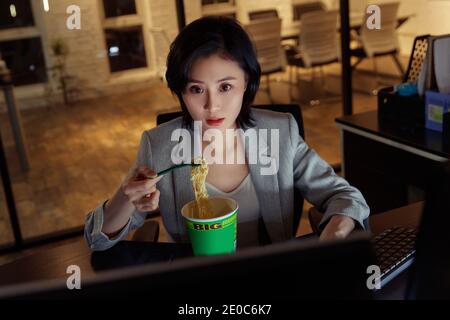 Young woman in the office to work overtime to eat instant noodles Stock Photo