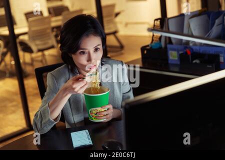 Young woman in the office to work overtime to eat instant noodles Stock Photo