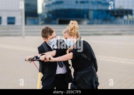 Education, childhood and people concept. Happy school children with backpacks and scooters outdoors in protective mask Stock Photo