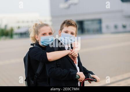 Education, childhood and people concept. Happy school children with backpacks and scooters outdoors in protective mask Stock Photo