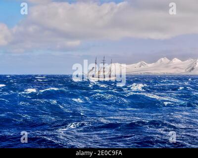 A three-masted schooner sailing in rough seas in Antarctica, traveling in a southerly direction past the snow-covered South Shetland Islands. Stock Photo