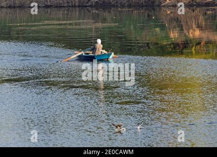 Traditional egyptian bedouin fisherman in rowing boat on river Nile fishing by riverbank Stock Photo