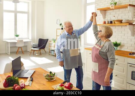 Happy senior couple dancing and having fun while cooking healthy meal in the kitchen Stock Photo