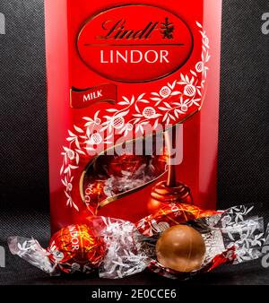 Closeup POV shot of an upright red box of Lindt Lindor wrapped chocolate truffles, with some showing in the box window, and two chocolates outside. Stock Photo