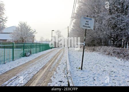 Snow covered road and park, snow on, tire tracks through snow, snow on trees on winter day in Manchester, England Stock Photo