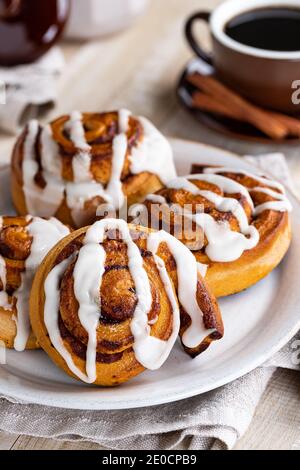 Cinnamon rolls with white icing on a plate and cup of coffee in background Stock Photo