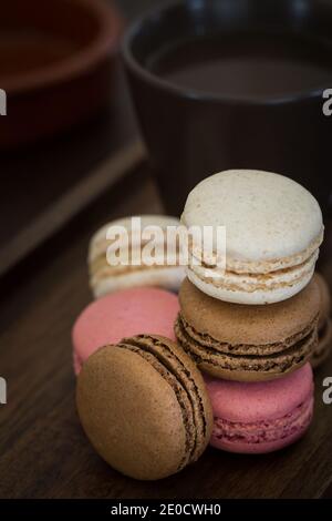 A close up of a stack of colourful Macaroons or Macarons including pink, chocolate and Vanilla with a cup of coffee Stock Photo